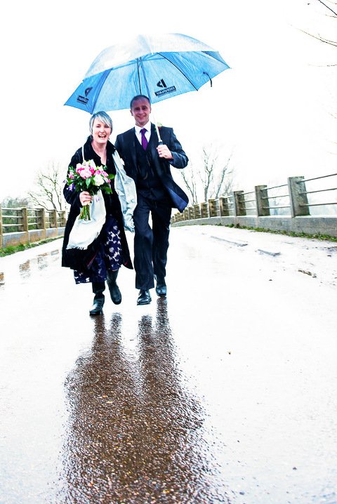 Bride and Groom running over bridge in the rain