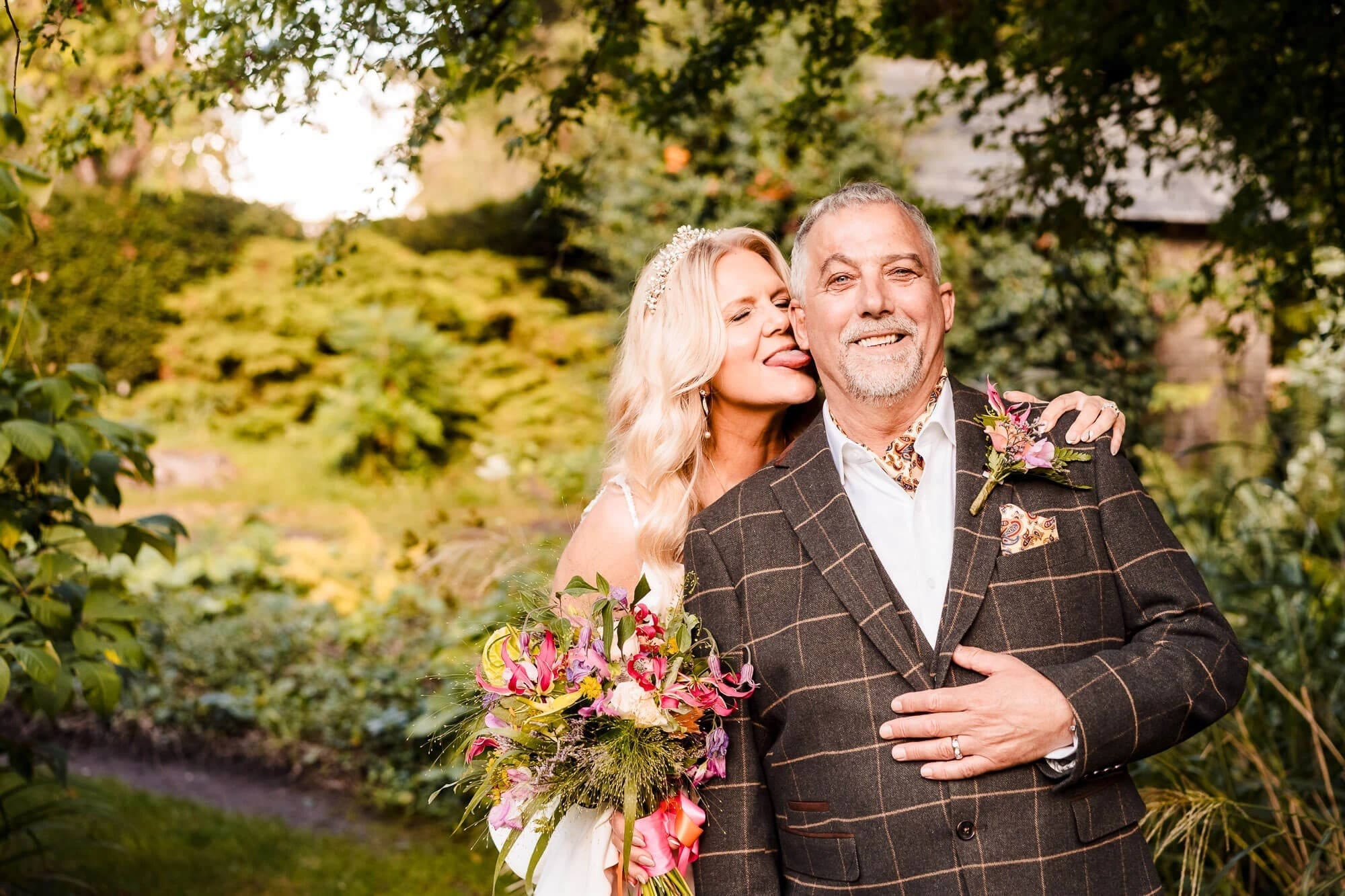 Couple posing together in a garden, woman kissing man's cheek while he smiles at camera — Wedding at South Farm, Cambridgeshire