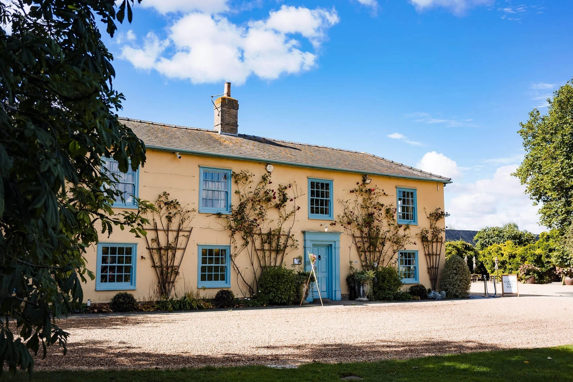 A cream-colored Georgian house stands in afternoon sunlight, framed by mature climbing ivy and manicured grounds. — Wedding at South Farm, Cambridgeshire