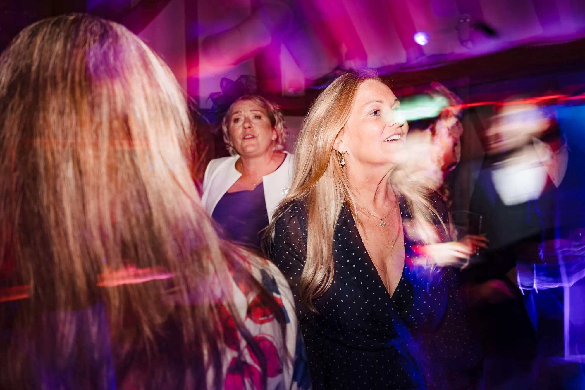 Woman dancing and smiling at a nightclub while surrounded by other guests — Wedding at South Farm, Cambridgeshire