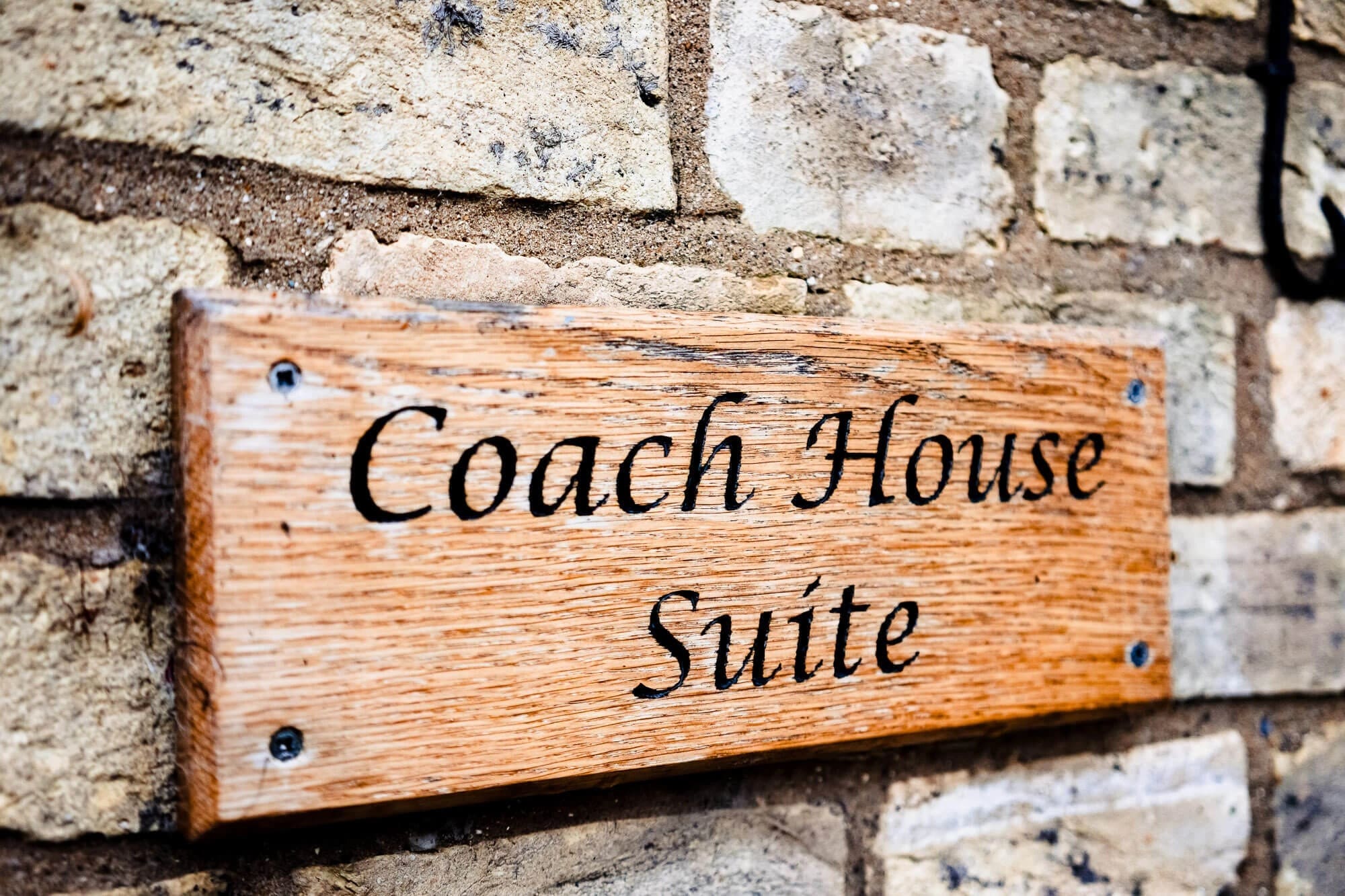 Wooden sign reading 'Coach House Suite' mounted on a stone wall. — Wedding at South Farm, Cambridgeshire