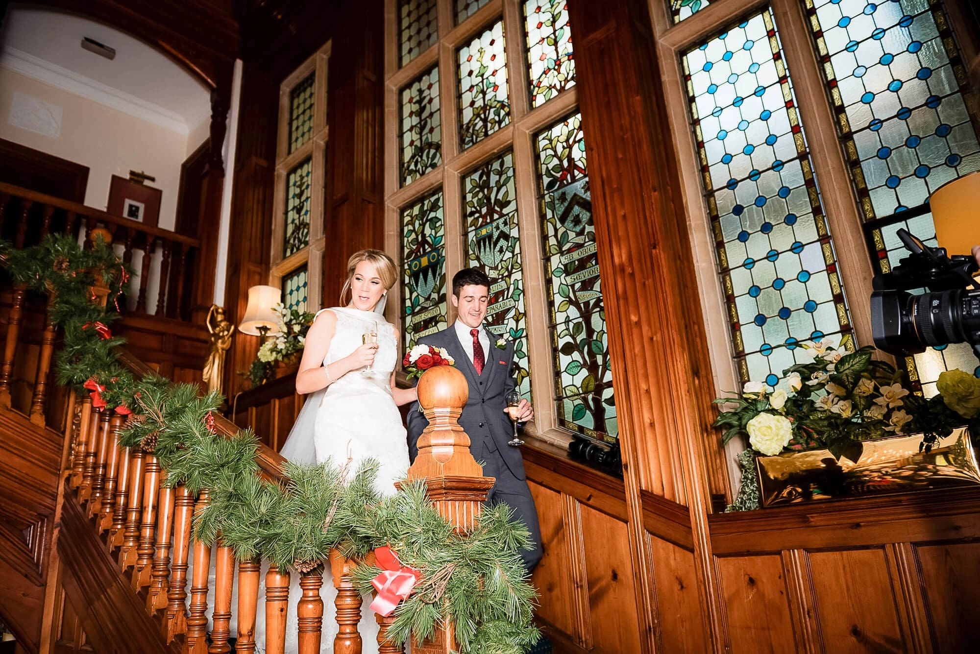 Bride and groom descending a wooden staircase decorated with garland for wedding portraits. — Wedding at Stanhill Court Hotel, Surrey