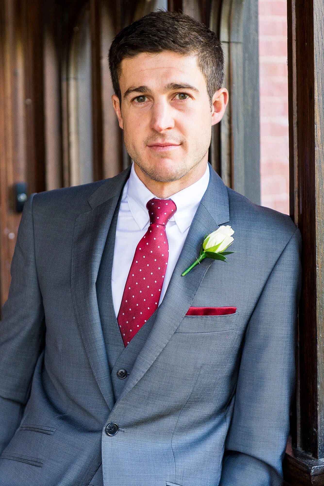 Groom standing for a formal portrait in an indoor hallway, wearing a boutonniere. — Wedding at Stanhill Court Hotel, Surrey