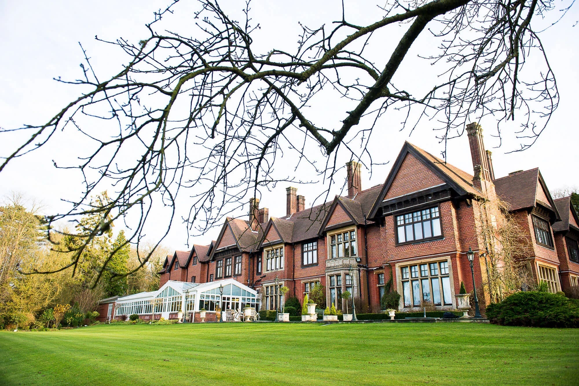 Manicured lawn and brick manor house viewed from the grounds, with bare tree branches overhead. — Wedding at Stanhill Court Hotel, Surrey