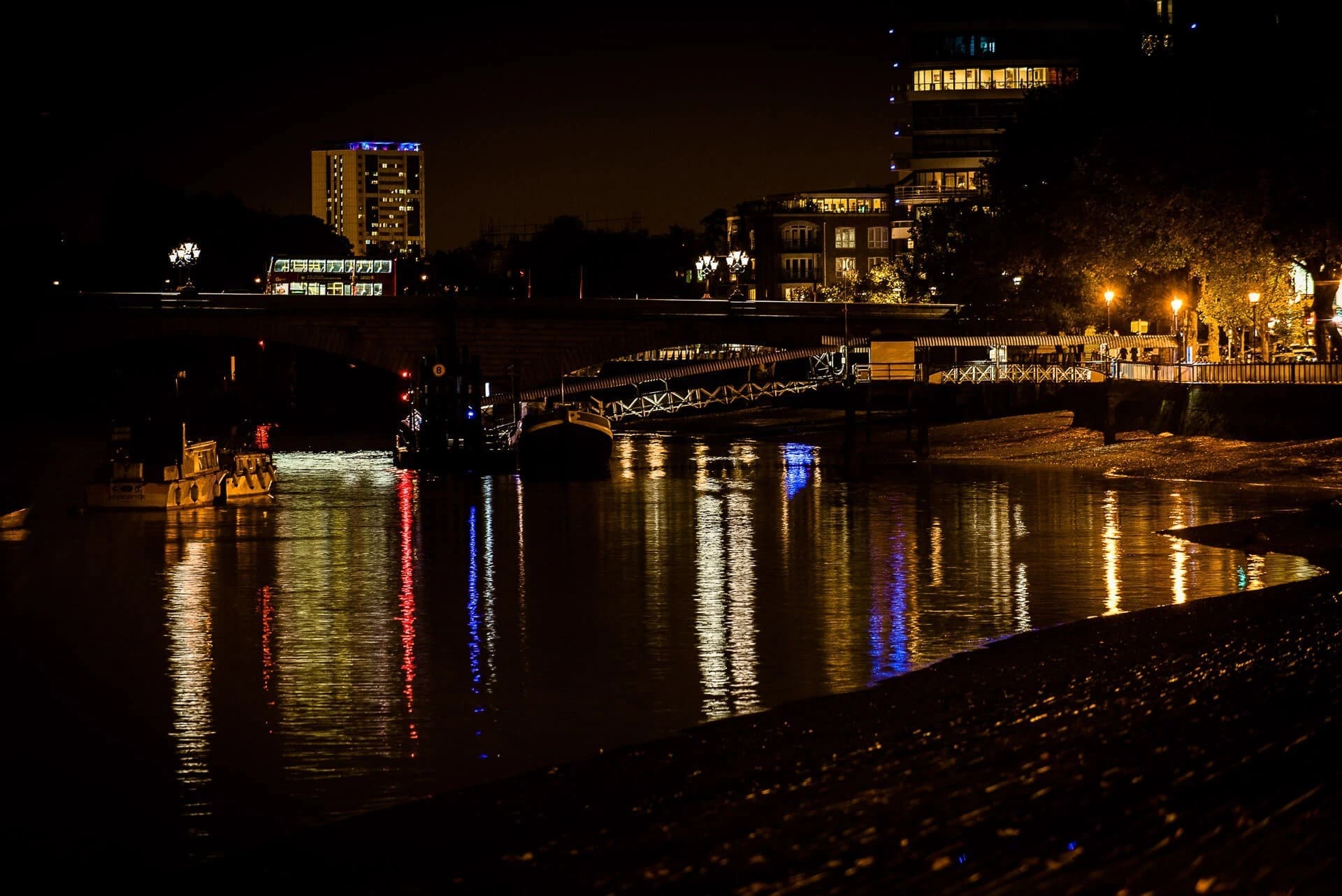 Nighttime cityscape reflected in still water, illuminated buildings and bridge creating golden and blue light patterns. — Wedding at The Lodge Hotel Putney, London