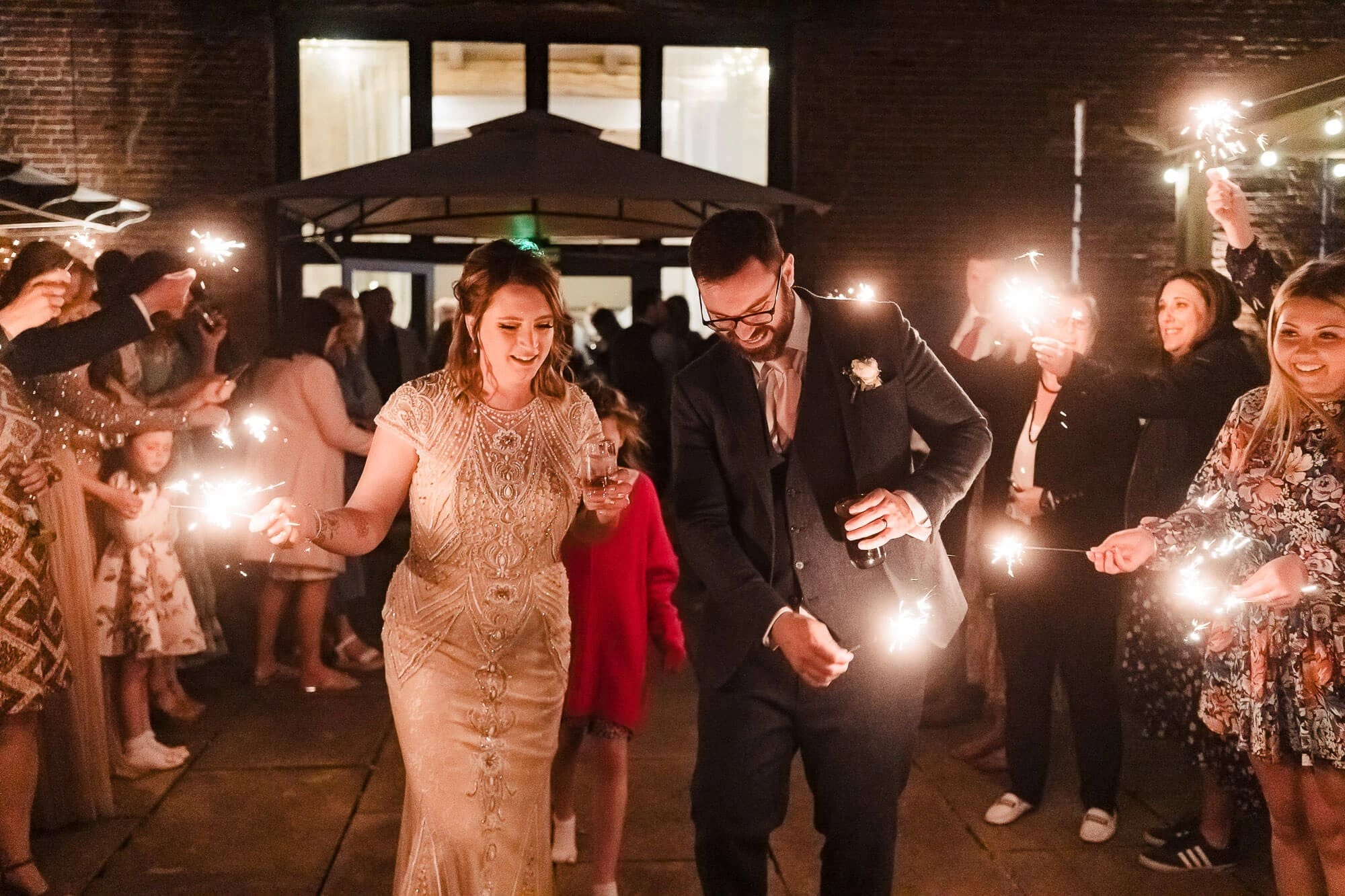 Newlyweds walk through a sparkler-lined tunnel as guests hold lit sparklers on either side. — Wedding at Manor Mews, Norfolk
