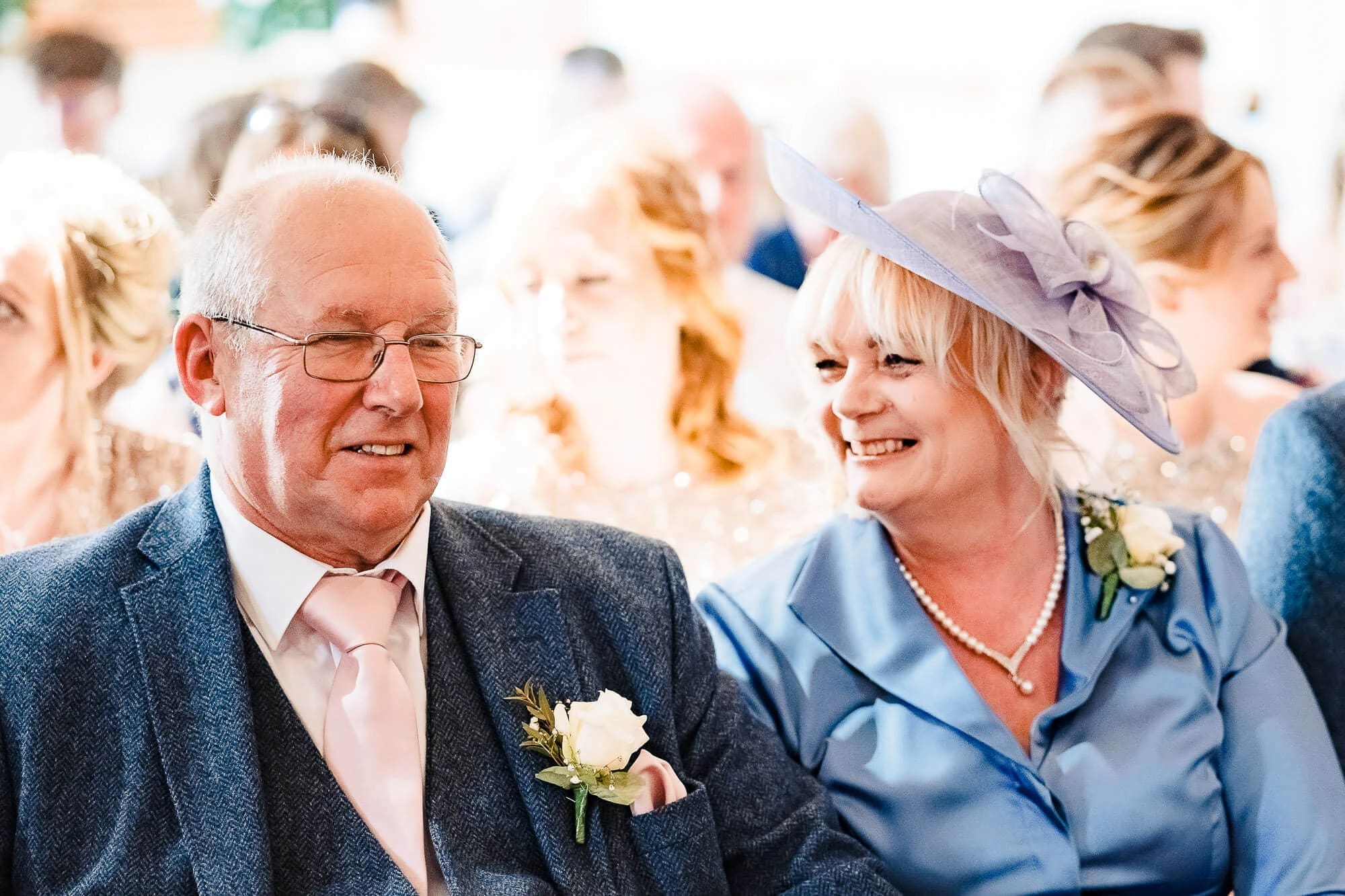 Older couple smiling together at an outdoor wedding celebration, the man in a blazer with boutonniere and woman in a hat. — Wedding at Manor Mews, Norfolk