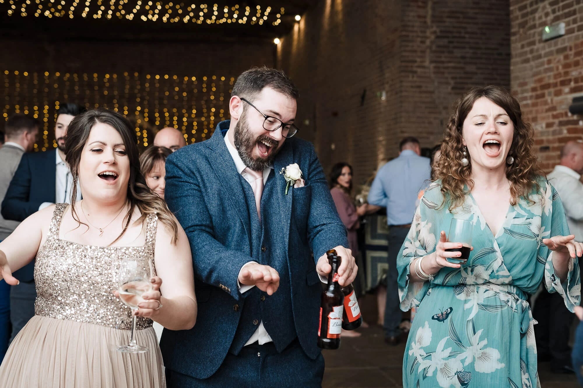 Three guests laughing and dancing together at a wedding reception, holding drinks and celebrating. — Wedding at Manor Mews, Norfolk