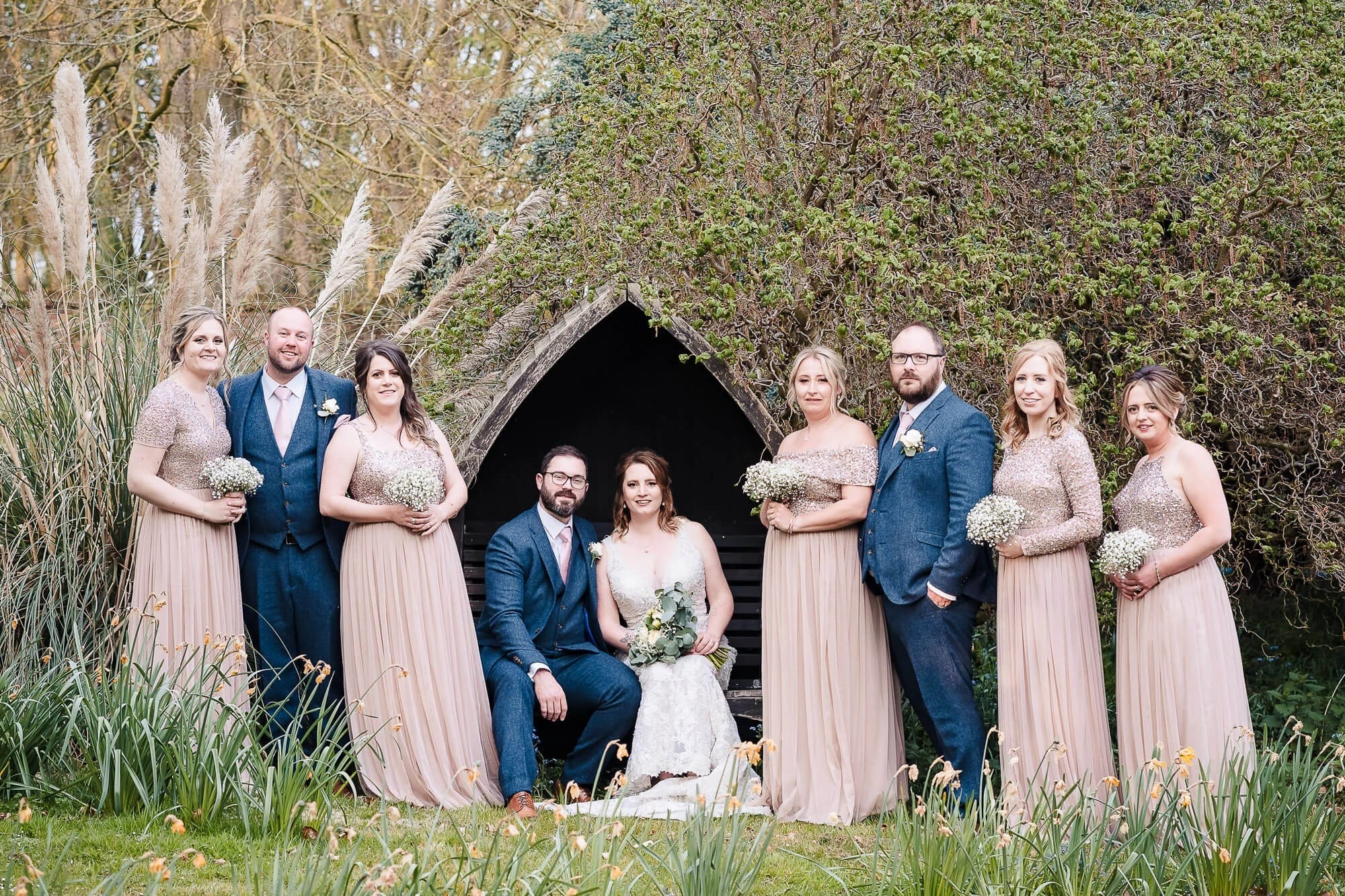 Wedding party posing together in front of a natural archway formed by ivy-covered trees and branches. — Wedding at Manor Mews, Norfolk