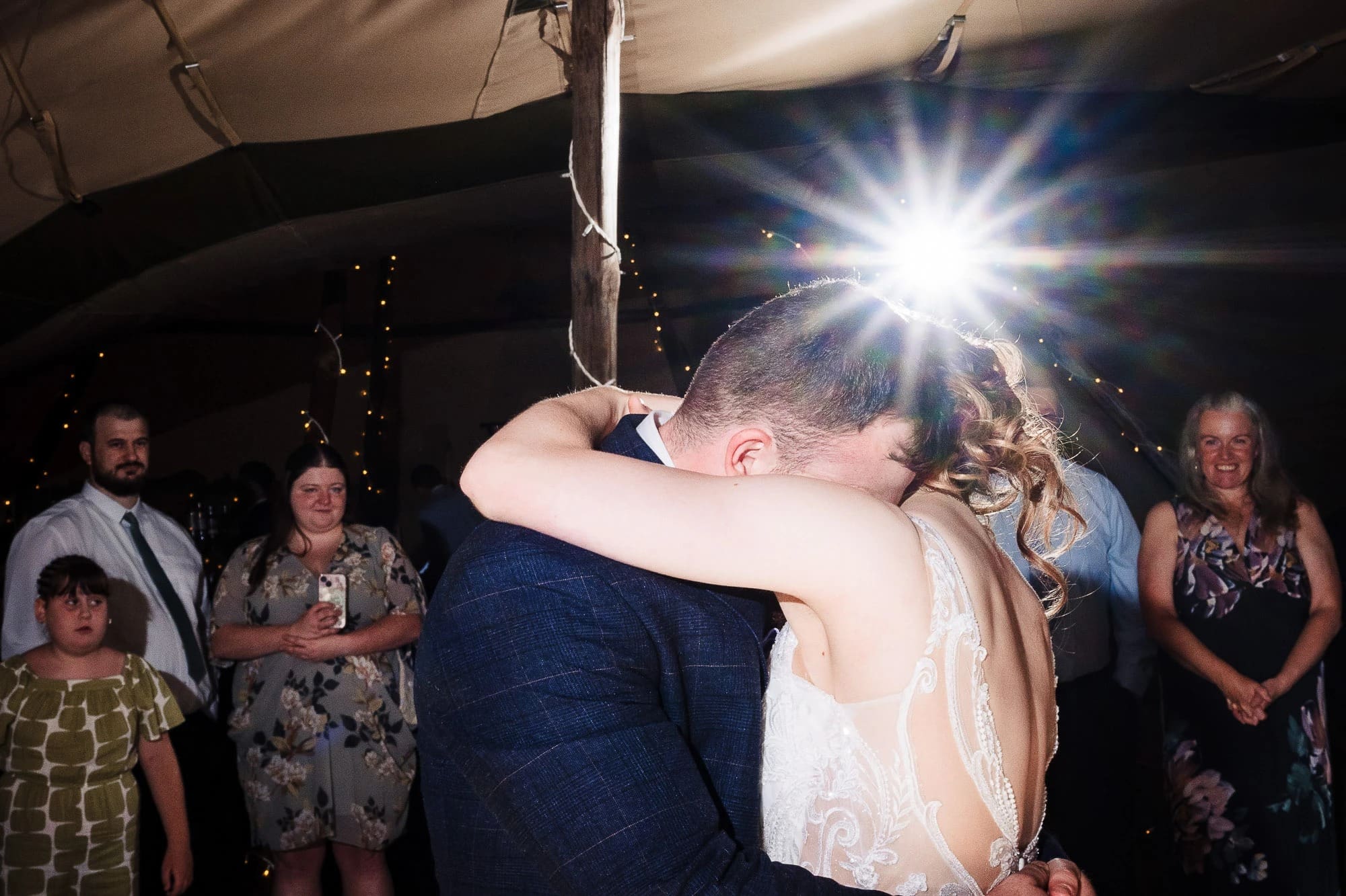 Bride and groom embracing during first dance at reception under bright spotlight. — Wedding at Moulton Parish Church, Northamptonshire