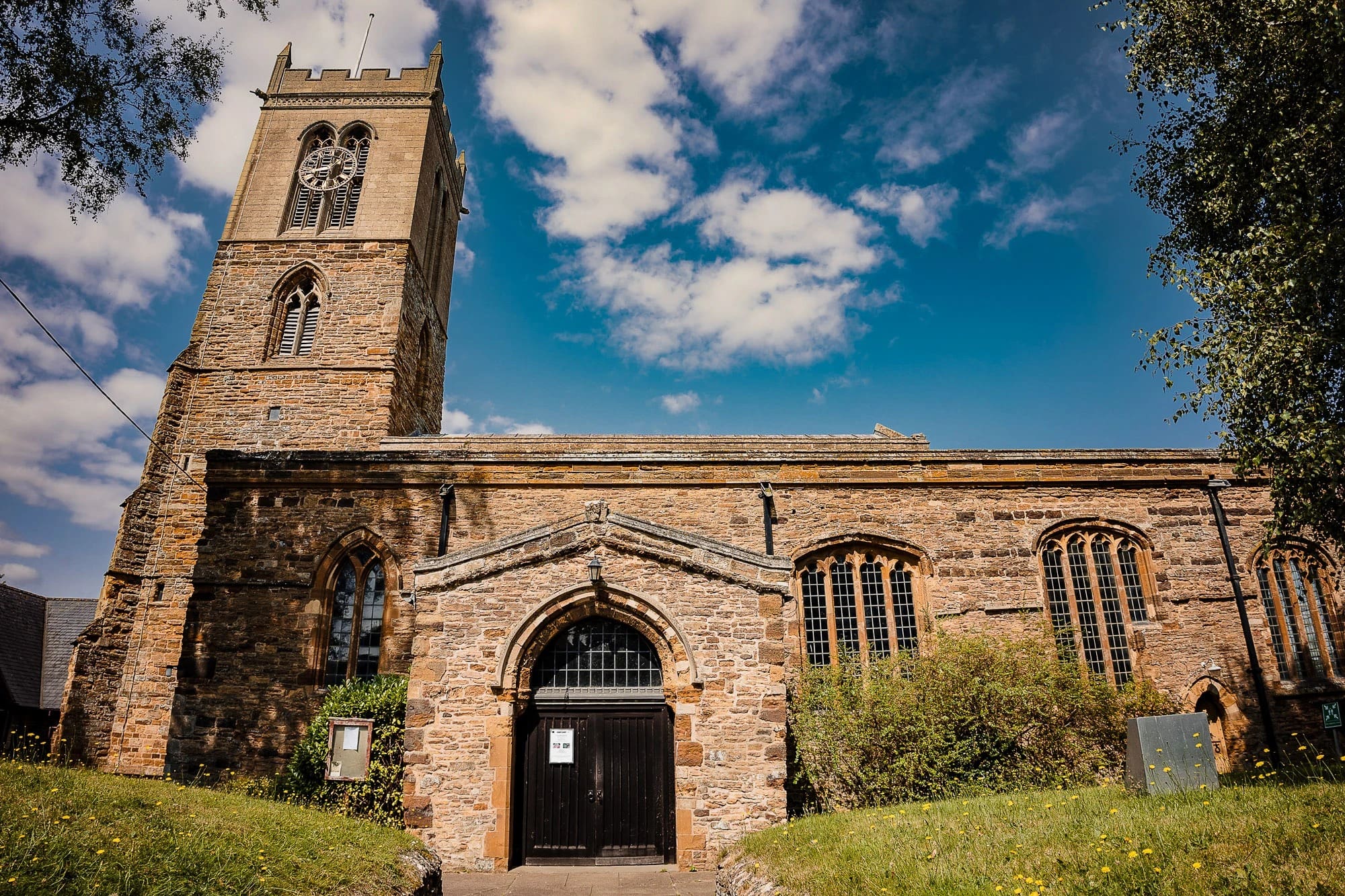 Stone church building standing in daylight under blue sky with white clouds. — Wedding at Moulton Parish Church, Northamptonshire
