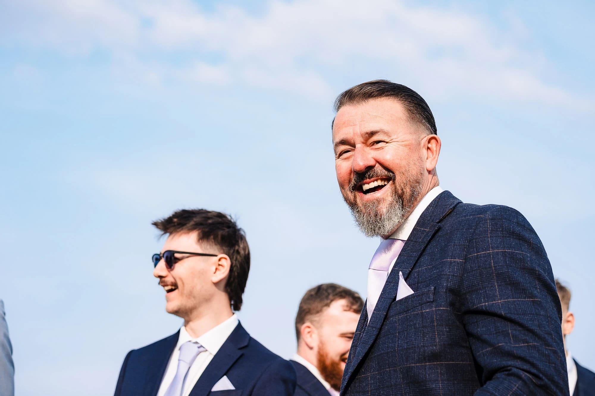 Three men standing outdoors, smiling and looking to the side during daytime. — Wedding at Moulton Parish Church, Northamptonshire