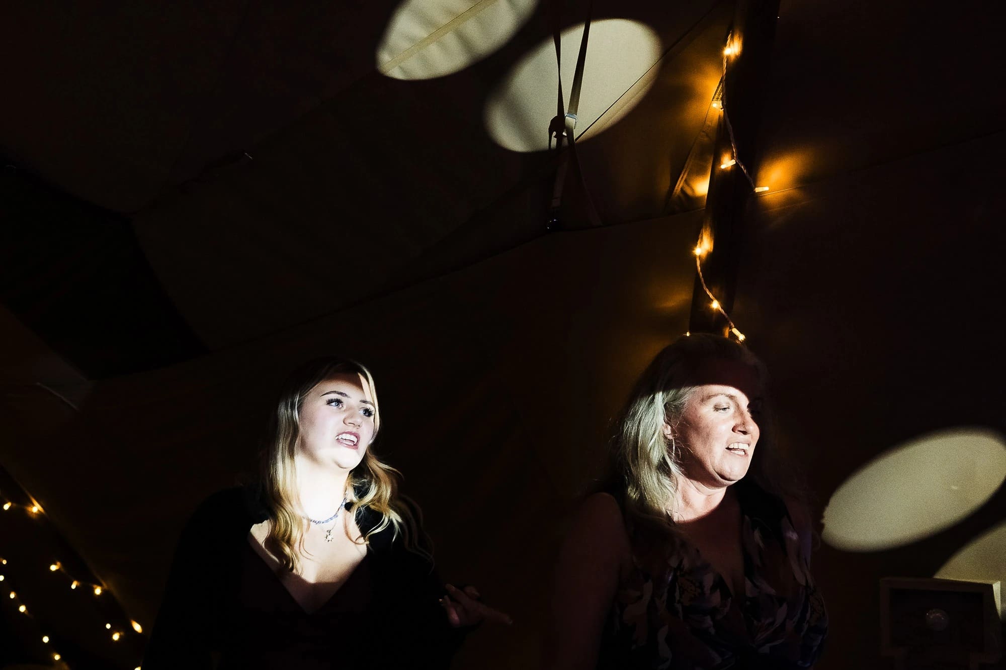 Two women looking upward at illuminated ceiling fixtures in a dark interior space. — Wedding at Moulton Parish Church, Northamptonshire