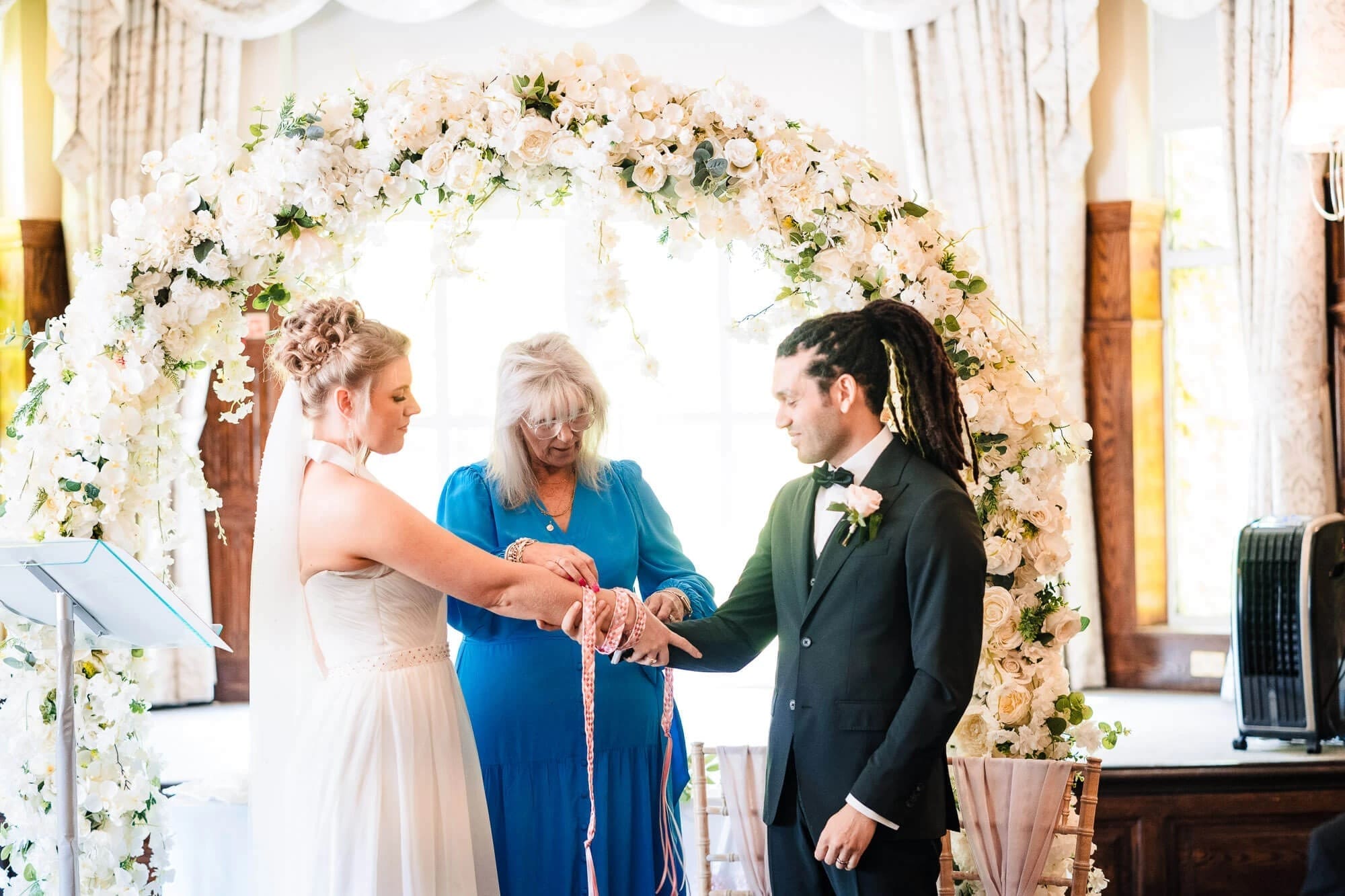 Bride and groom exchanging rings at the altar while officiant guides their hands together. — Wedding at Sprowston Manor Hotel, Norfolk