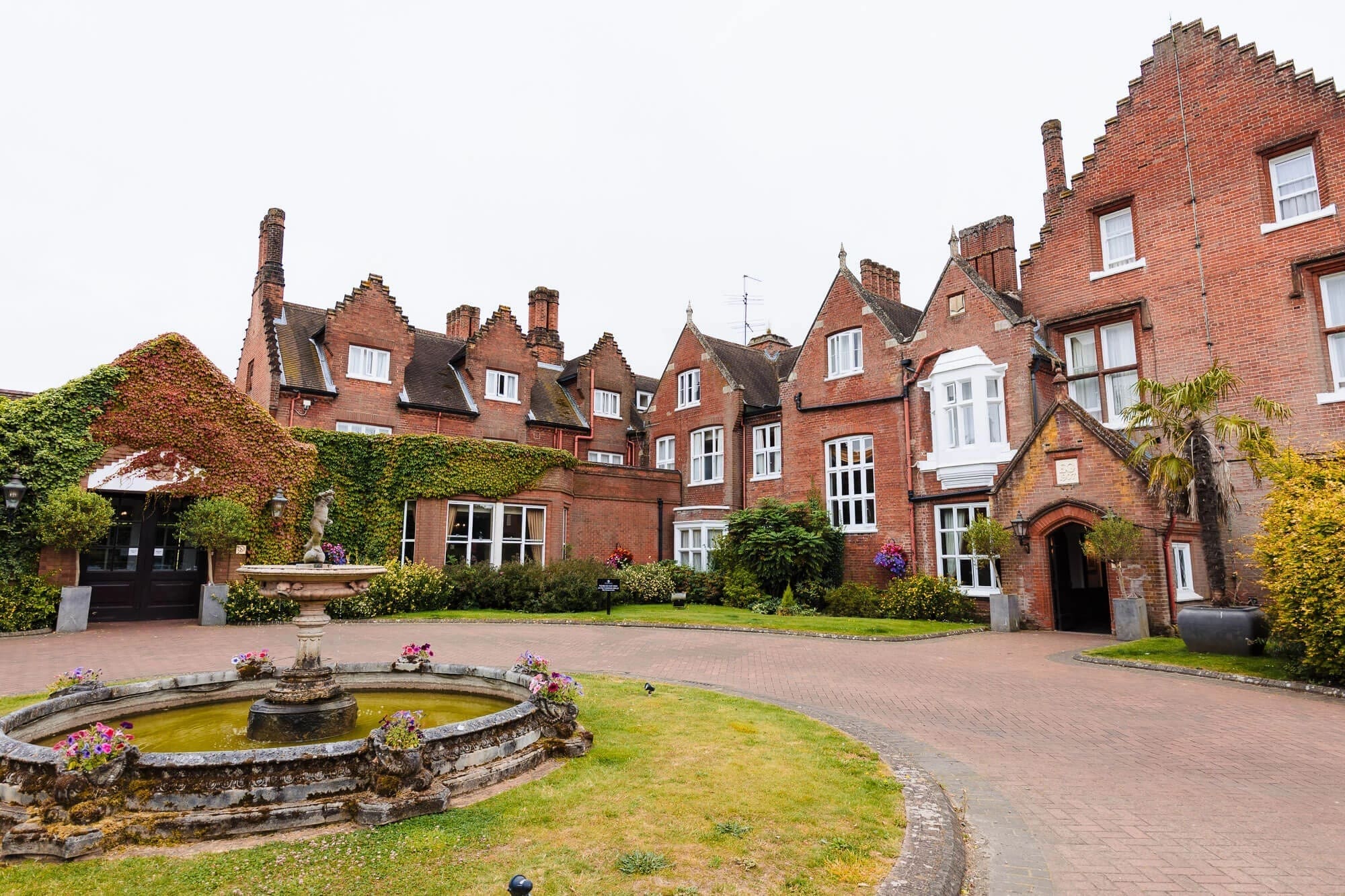 Exterior view of a grand brick manor house with manicured grounds and a central fountain. — Wedding at Sprowston Manor Hotel, Norfolk