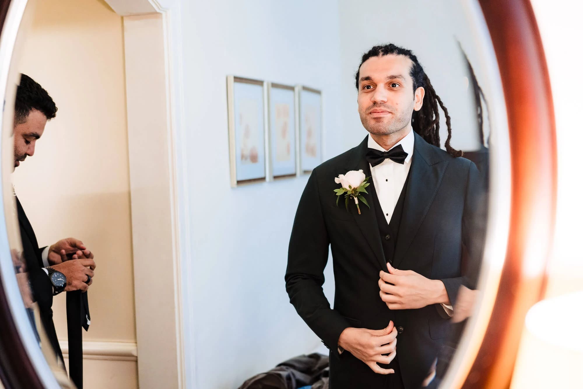 Groom adjusting his jacket while another man watches in a hallway mirror reflection. — Wedding at Sprowston Manor Hotel, Norfolk