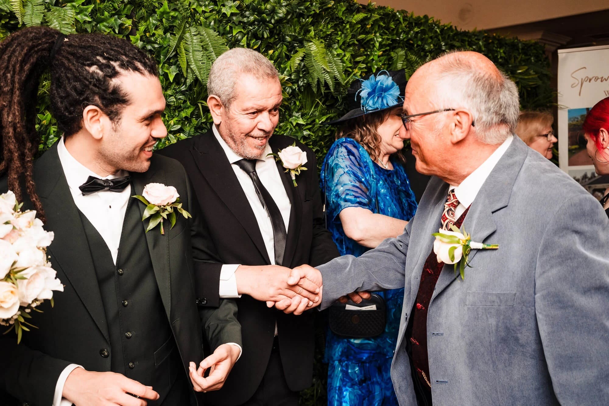 Groom shaking hands with a guest while another guest watches in the background at a reception. — Wedding at Sprowston Manor Hotel, Norfolk