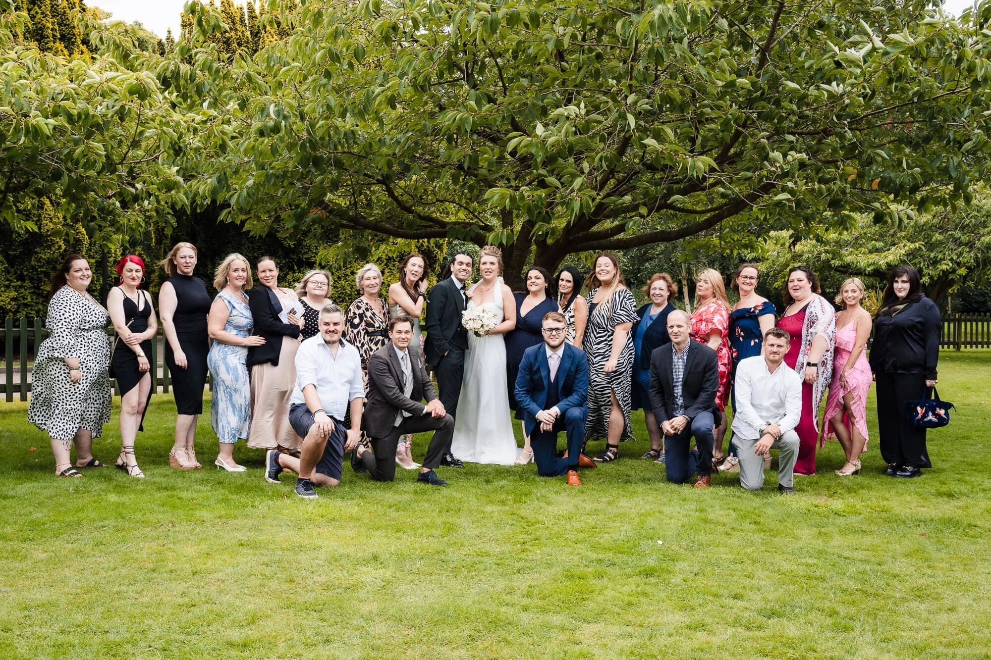 Large wedding party posing together on a manicured lawn beneath mature trees. — Wedding at Sprowston Manor Hotel, Norfolk