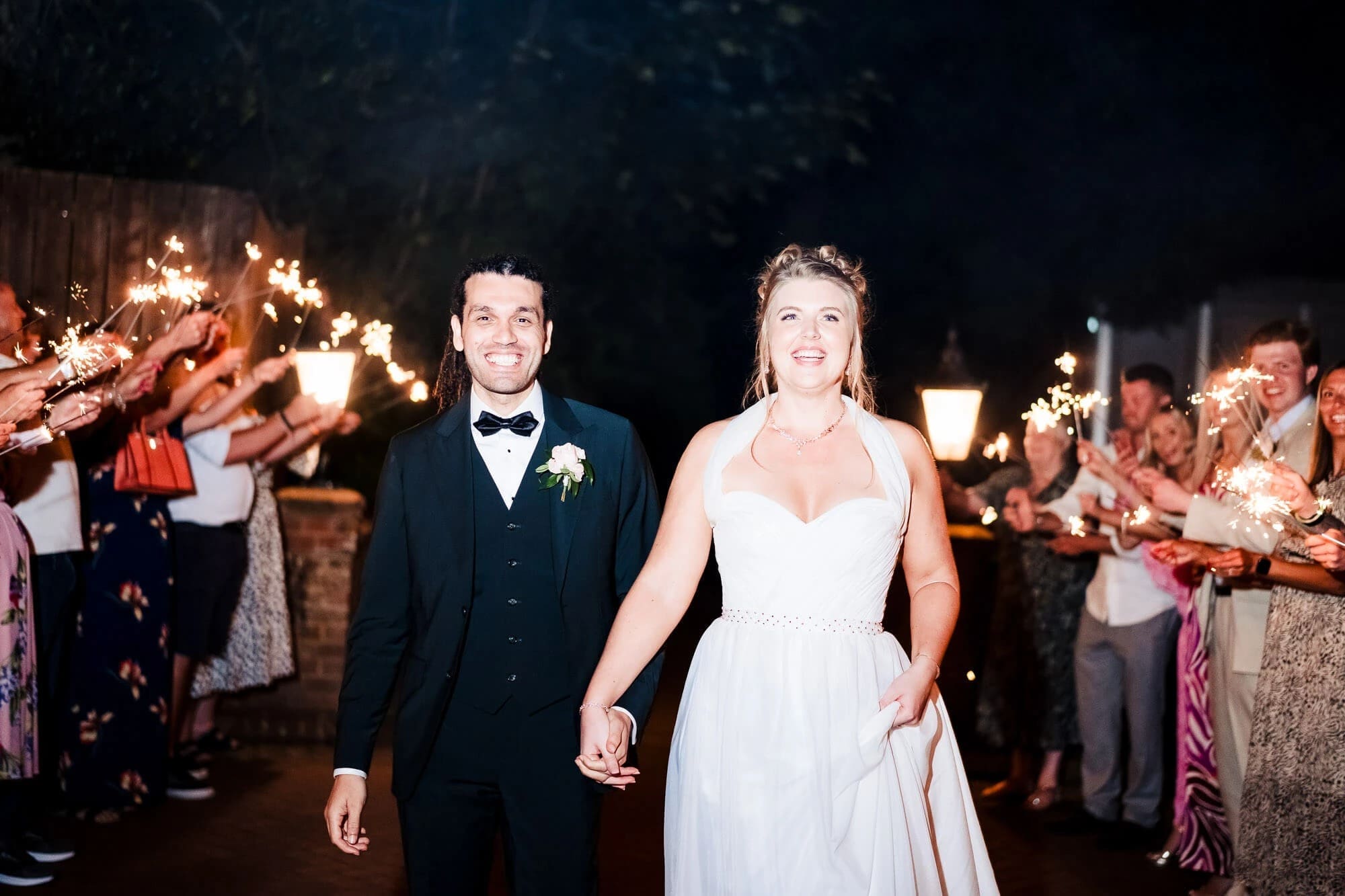 Newlyweds walk hand-in-hand through a sparkler-lined tunnel as guests cheer. — Wedding at Sprowston Manor Hotel, Norfolk